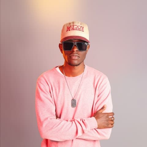 Josh Major in a pink sweater, cap and sunglasses against a pale pink wall